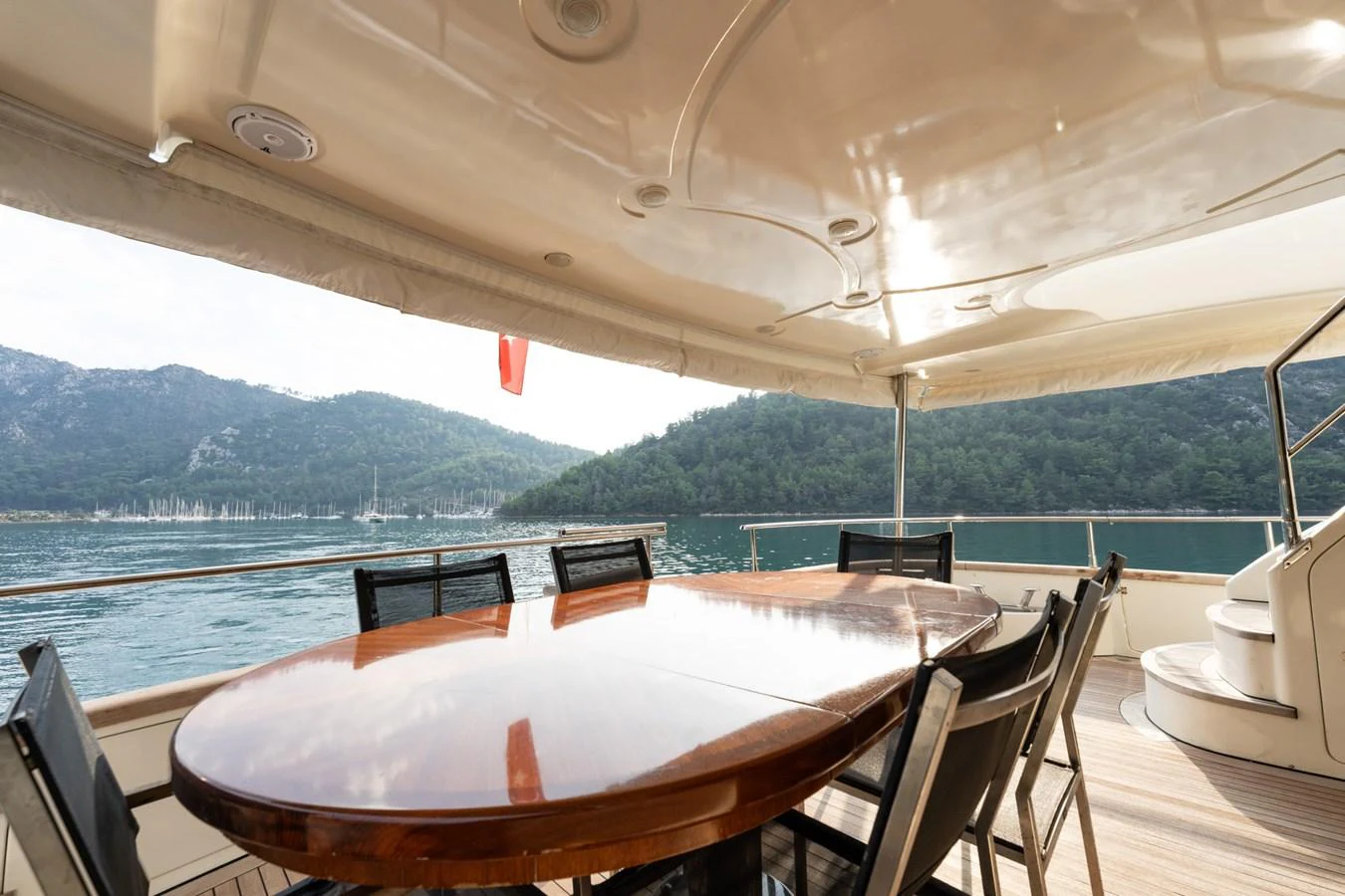 The aft deck features a polished wooden dining table with a scenic view of the surrounding waters and mountains. aboard SENIOR S Yacht for Sale
