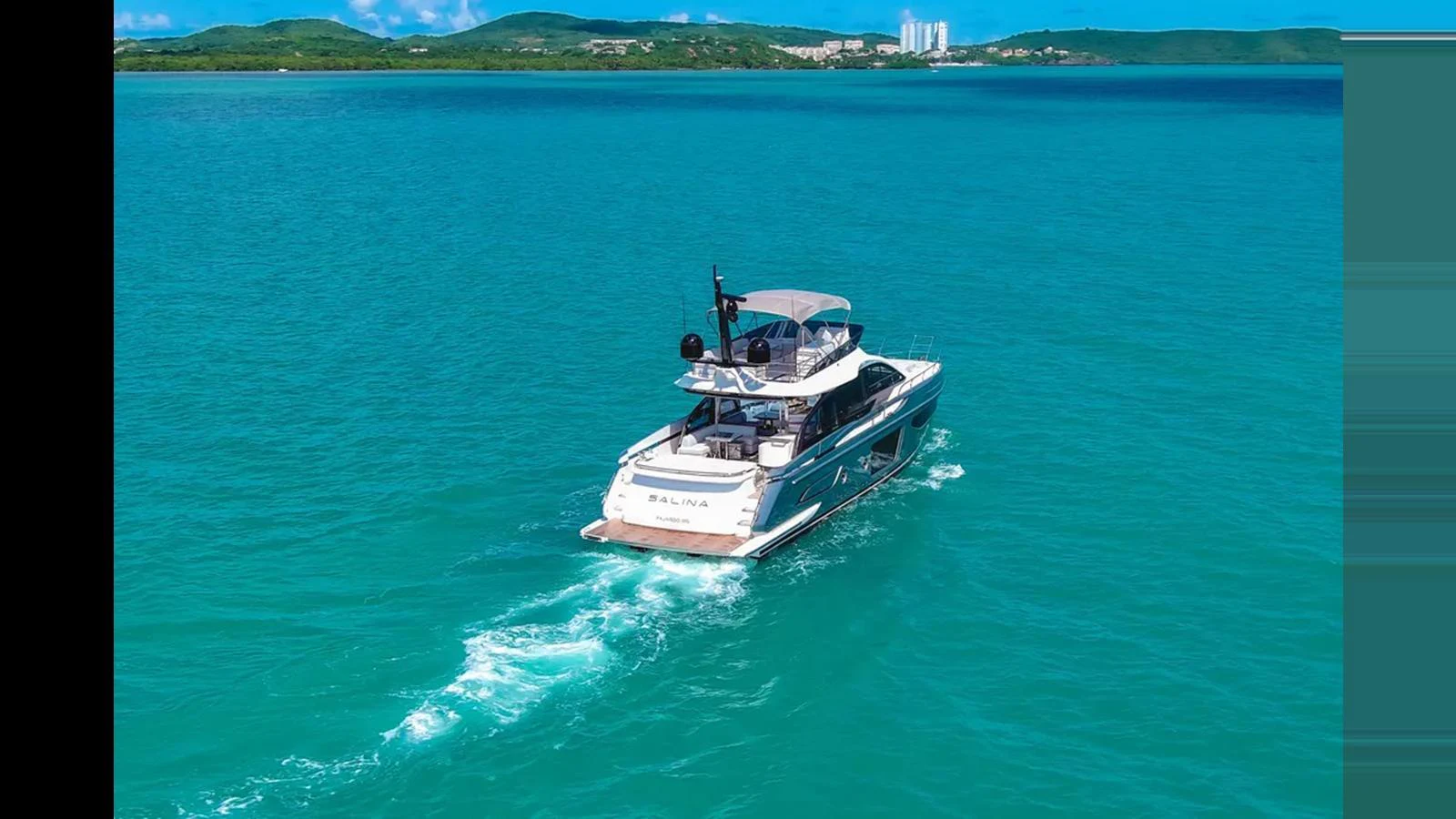 A sleek yacht cruises through clear turquoise waters with a scenic coastline in the background. aboard AZIMUT S7 Yacht for Sale