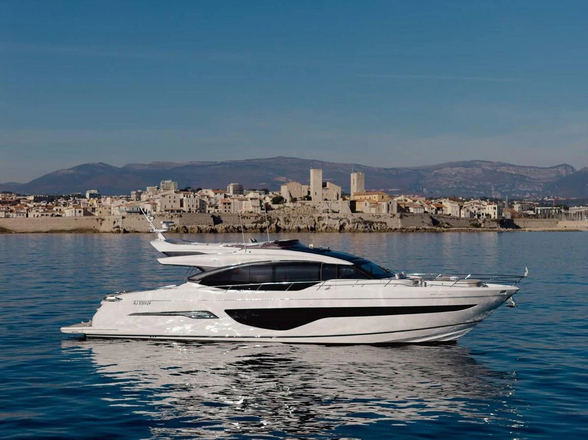 A sleek and modern yacht glides gracefully on calm waters with a historic coastal town in the background. aboard CAMILLE Yacht for Sale
