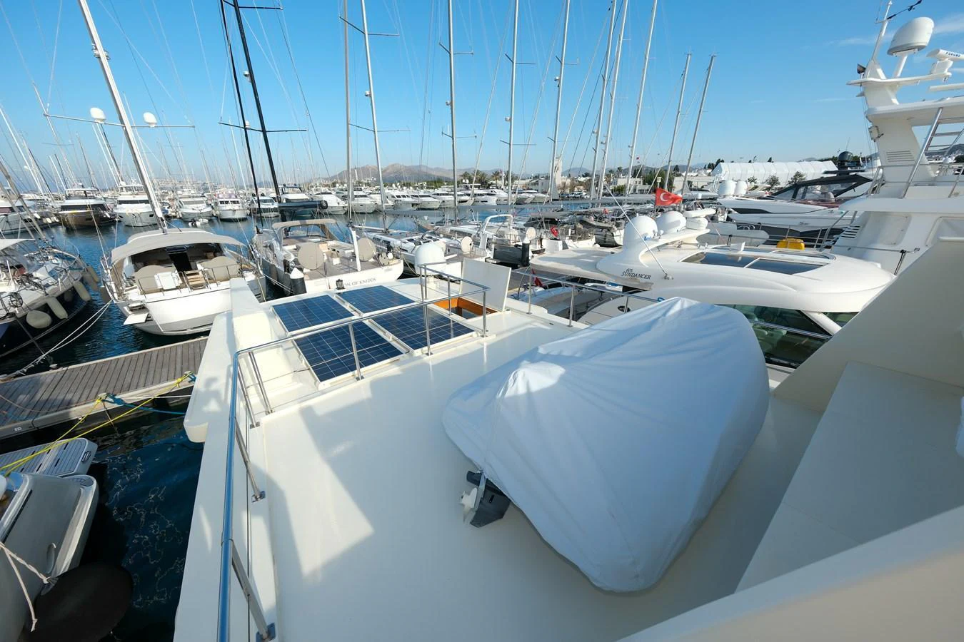 The yacht's upper deck offers a spacious area with a covered section, surrounded by a marina filled with other boats. aboard XANAX Yacht for Sale