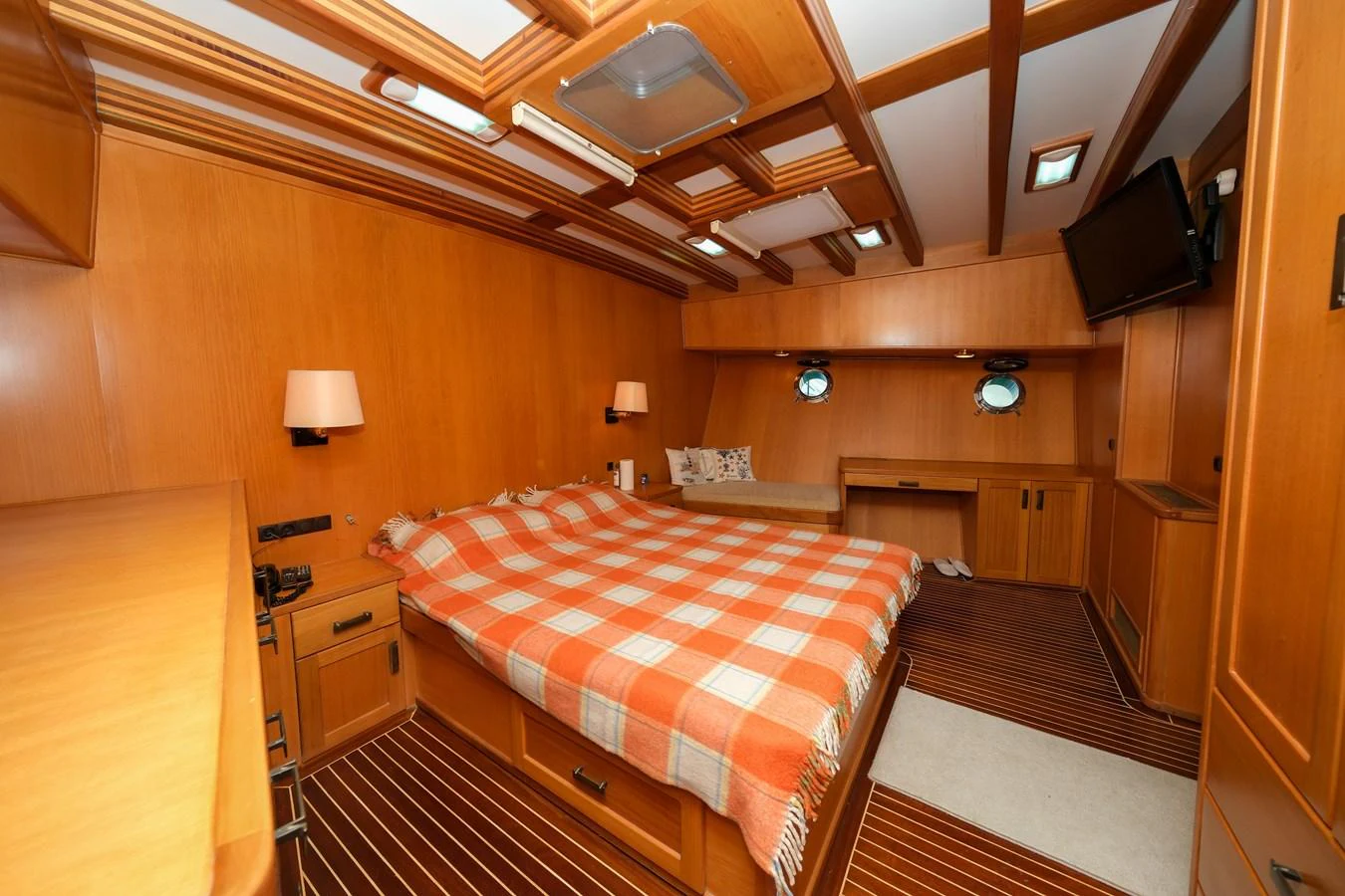 A cozy stateroom with warm wood paneling and a comfortable bed adorned with a checkered blanket. aboard XANAX Yacht for Sale