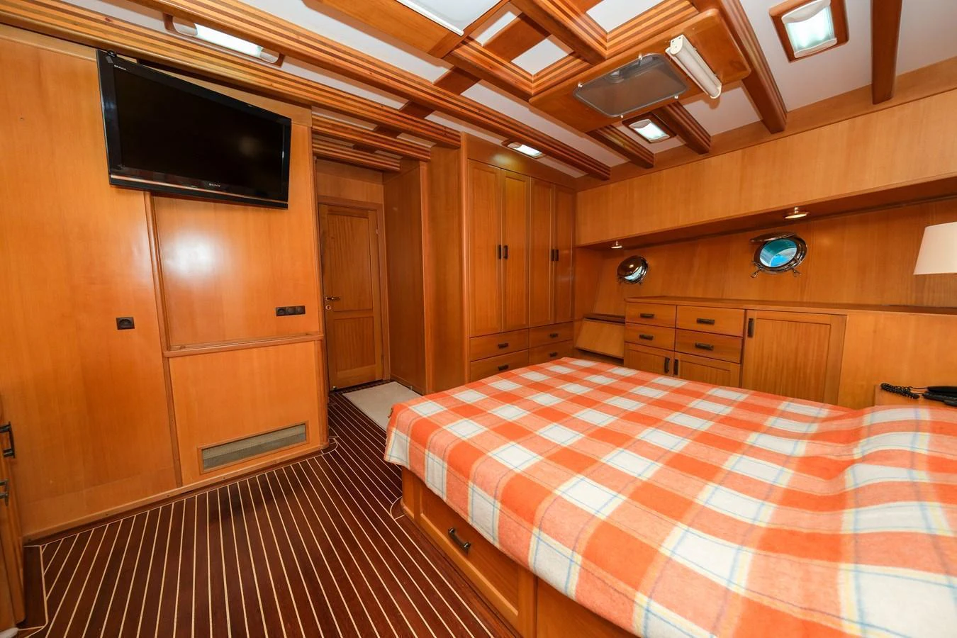 The stateroom features warm wood paneling, a comfortable bed with a checkered blanket, and ample storage space. aboard XANAX Yacht for Sale