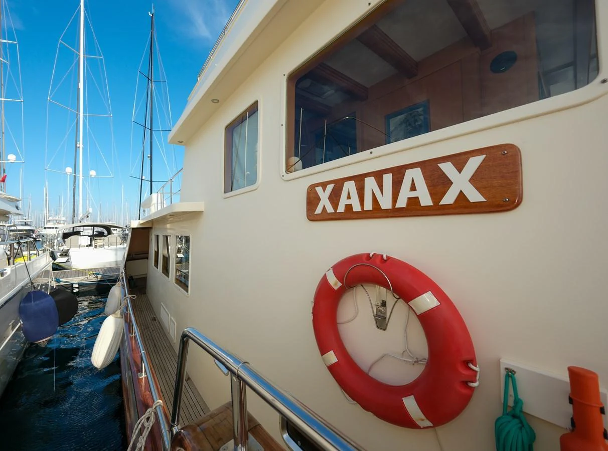 The yacht is docked at a marina, showcasing its side with a lifebuoy and a nameplate visible. aboard XANAX Yacht for Sale
