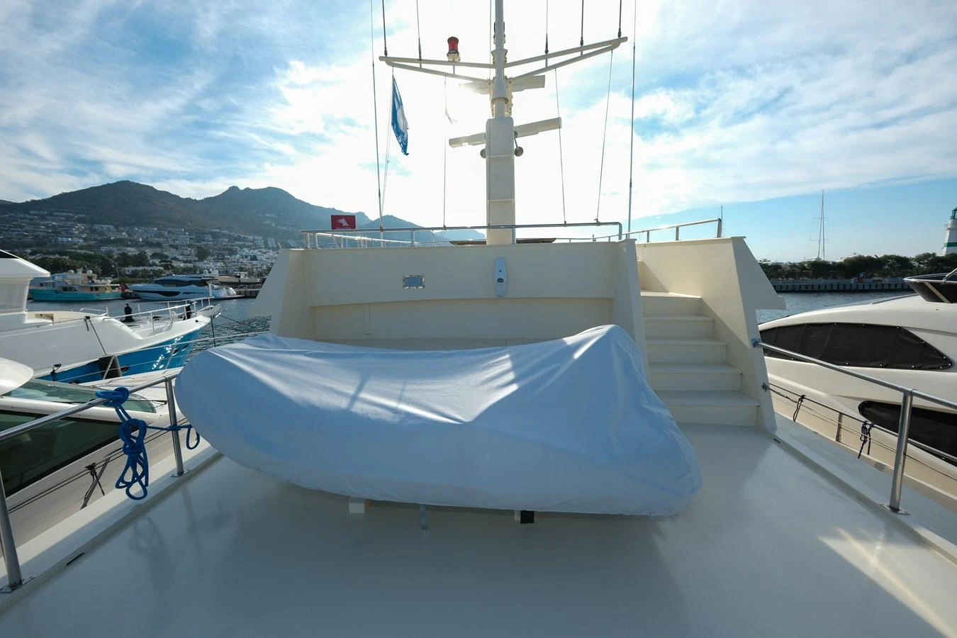 The aft deck features a covered tender with stairs leading up to the upper deck, set against a scenic marina backdrop. aboard XANAX Yacht for Sale