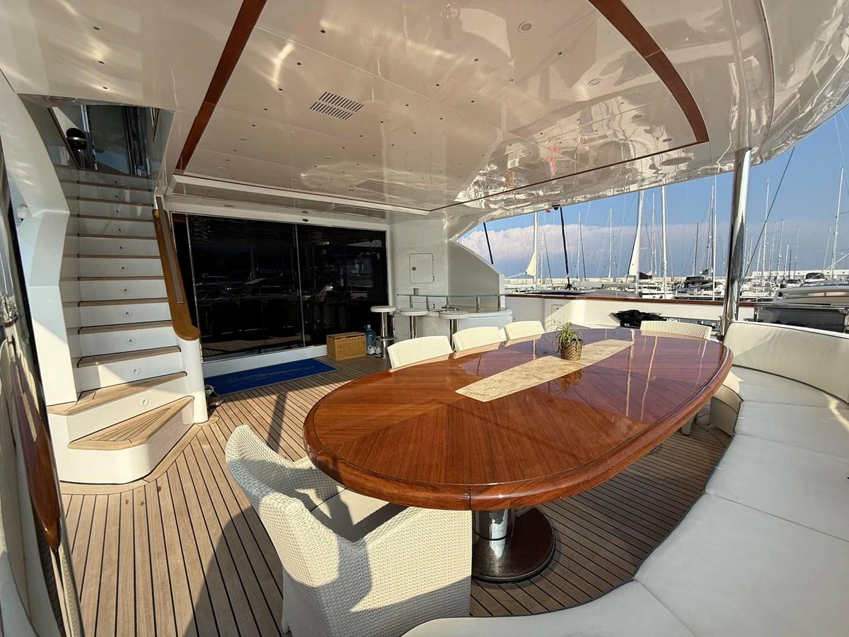 The aft deck features a spacious dining area with a polished wooden table and comfortable seating, perfect for alfresco meals. aboard COF Yacht for Sale