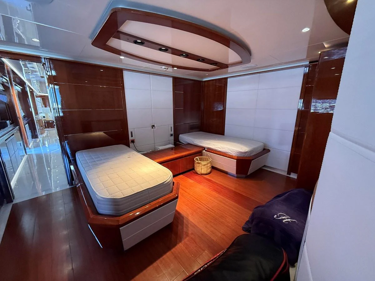 The guest stateroom features two single beds with elegant wood paneling and modern lighting. aboard COF Yacht for Sale