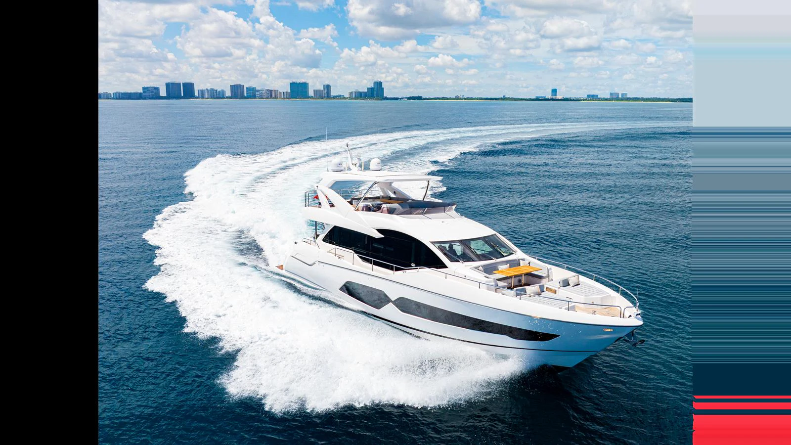 A sleek yacht cruises swiftly on open waters with a city skyline in the background. aboard STEELN Yacht for Sale