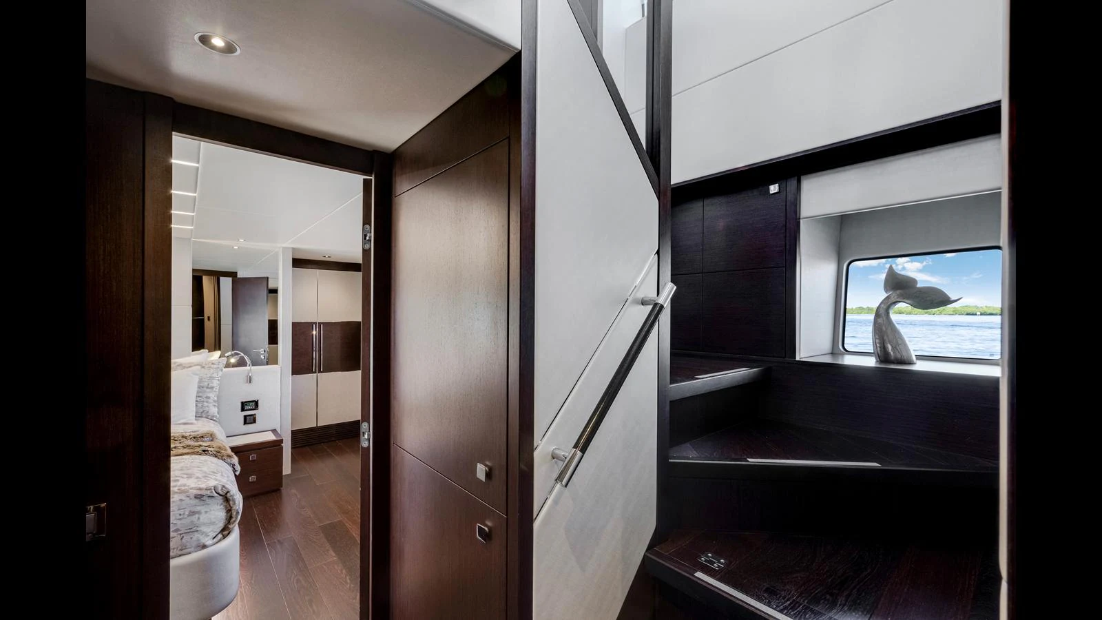 A sleek and modern staircase area with dark wood finishes and ample natural light from the window. aboard STEELN Yacht for Sale