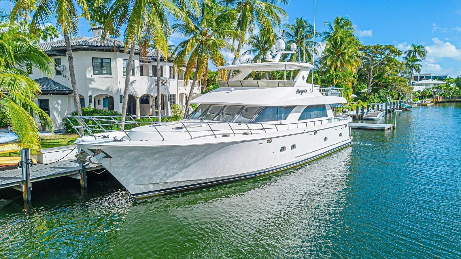 A luxurious yacht is docked in a serene waterfront setting, surrounded by palm trees and elegant homes. aboard MARGARITA Yacht for Sale