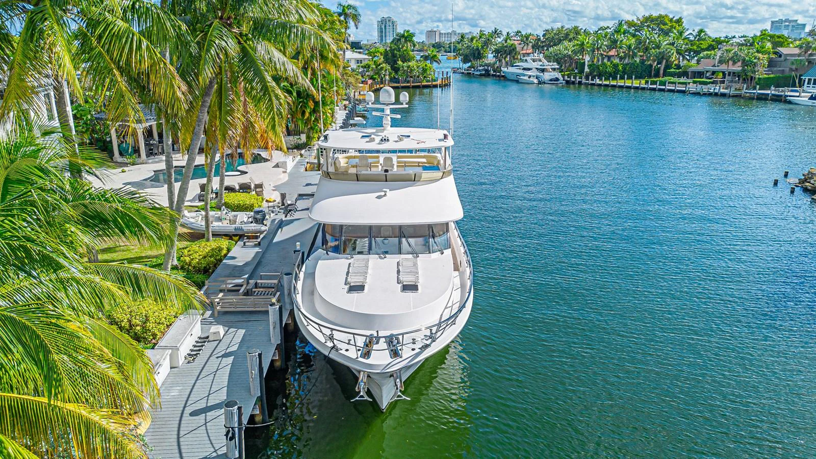 A luxurious yacht is docked in a serene waterfront setting, surrounded by lush greenery and palm trees. aboard MARGARITA Yacht for Sale