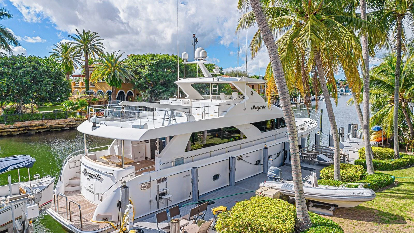 A luxurious yacht is docked in a picturesque marina surrounded by lush greenery and palm trees. aboard MARGARITA Yacht for Sale