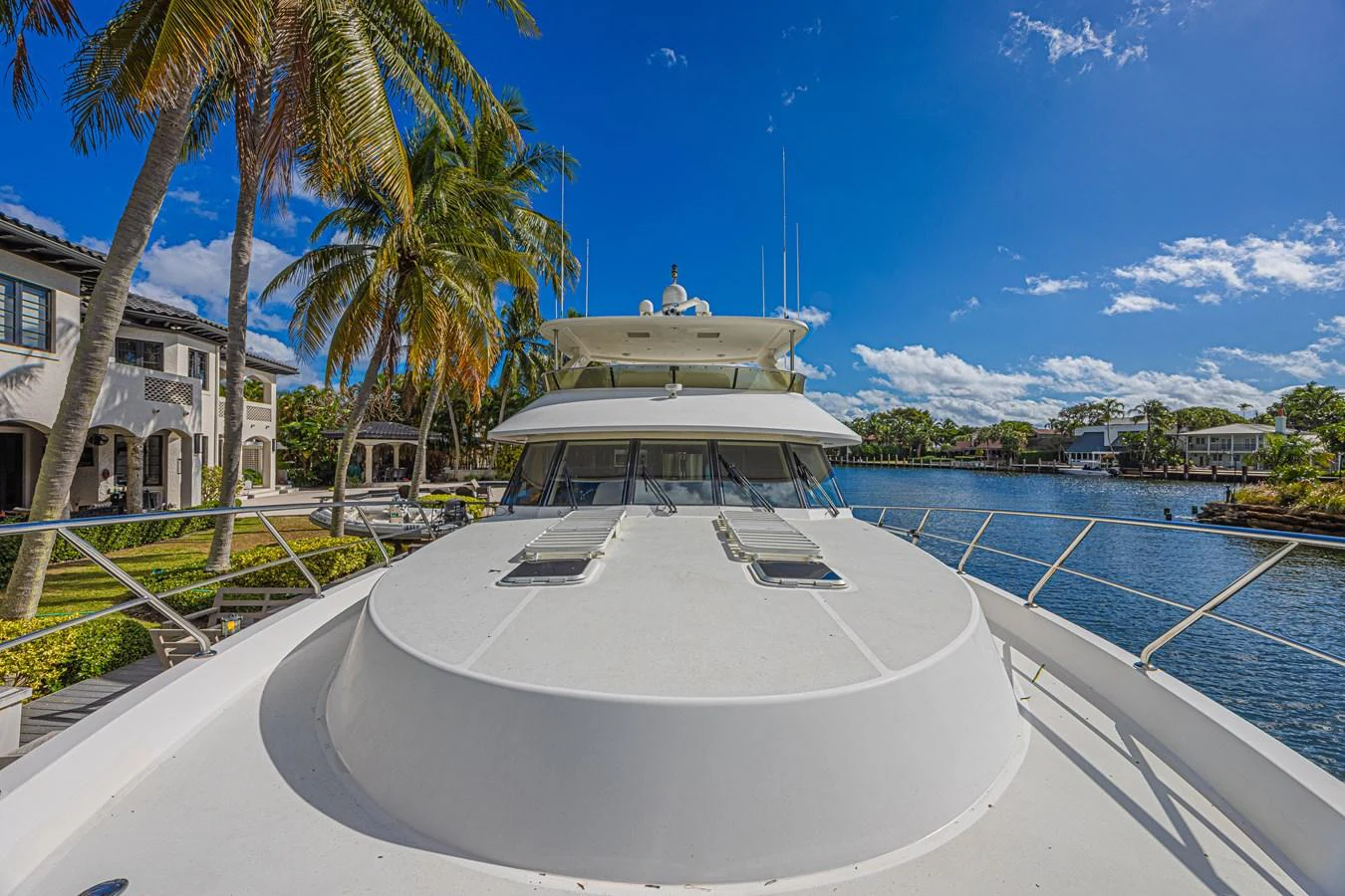 The yacht is docked in a serene waterfront neighborhood with clear blue skies and lush palm trees in the background. aboard MARGARITA Yacht for Sale
