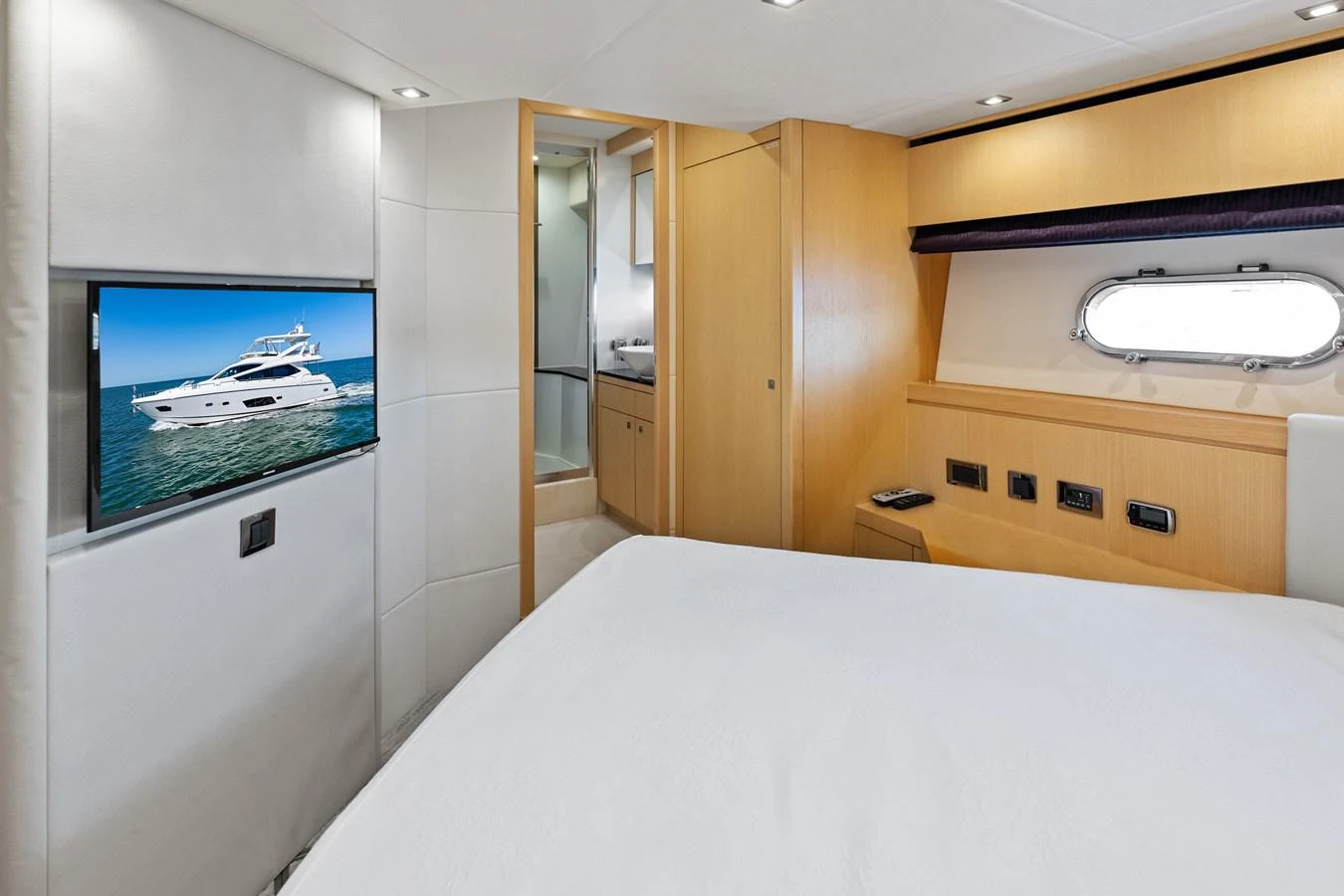 A cozy stateroom featuring a comfortable bed, a wall-mounted TV, and a porthole window for natural light. aboard IT'S ENOUGH Yacht for Sale