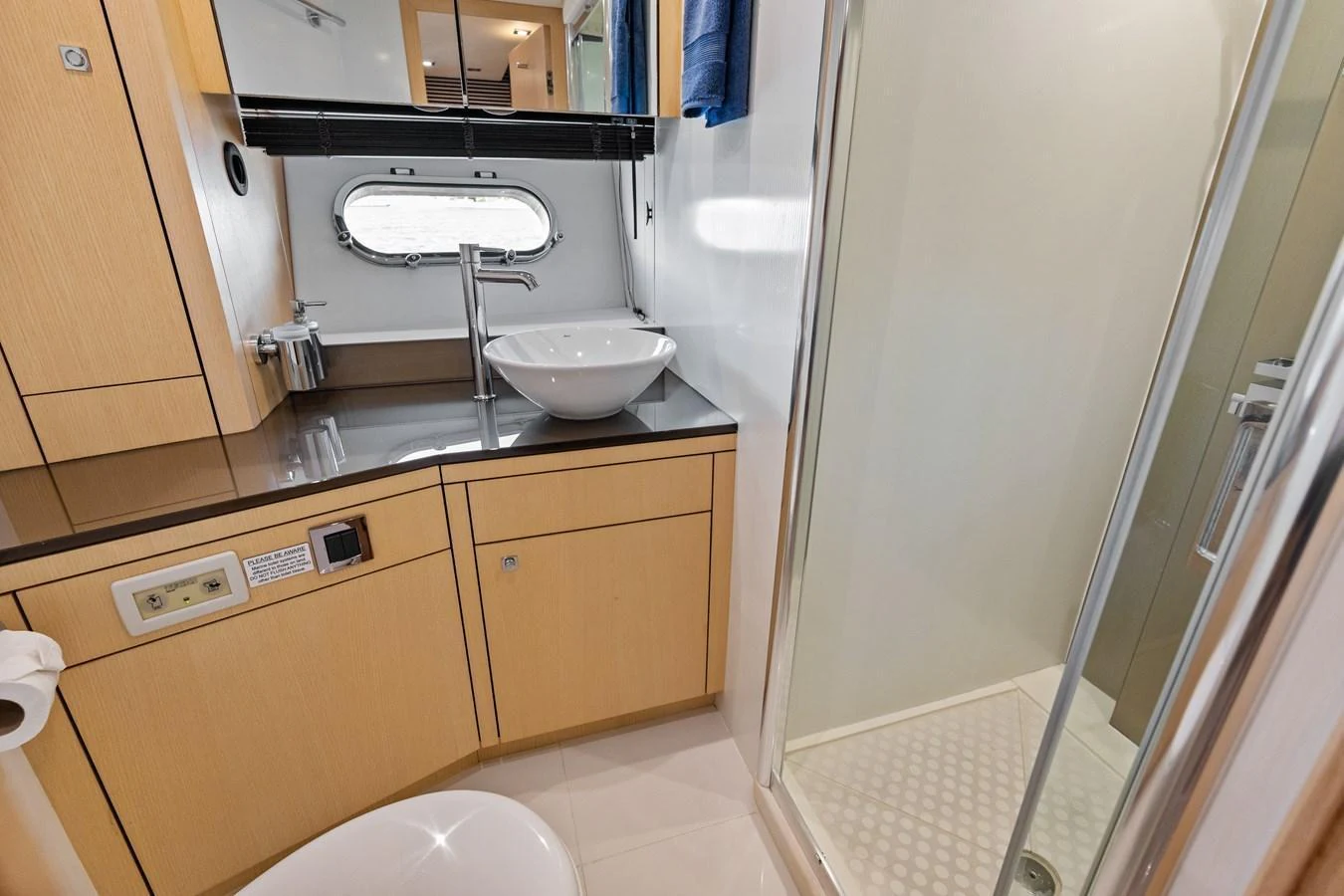 A modern yacht bathroom featuring a sleek sink, a porthole window, and a glass-enclosed shower. aboard IT'S ENOUGH Yacht for Sale