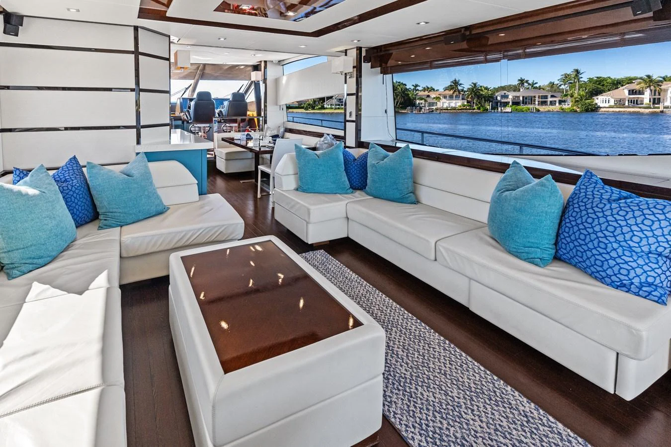 The salon features luxurious seating with blue accent pillows and large windows offering stunning water views. aboard IT'S ENOUGH Yacht for Sale