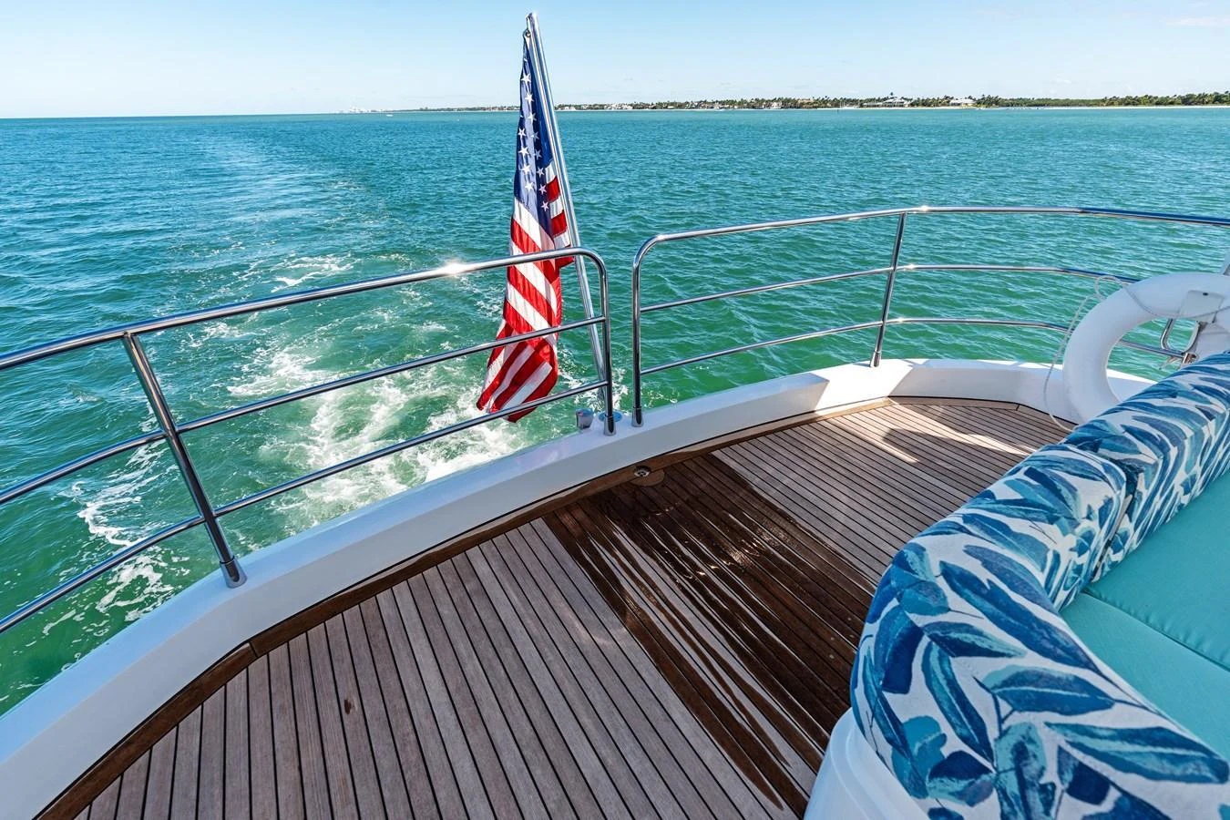 The aft deck offers a serene view of the open water, complemented by a comfortable seating area and a patriotic flag. aboard IT'S ENOUGH Yacht for Sale