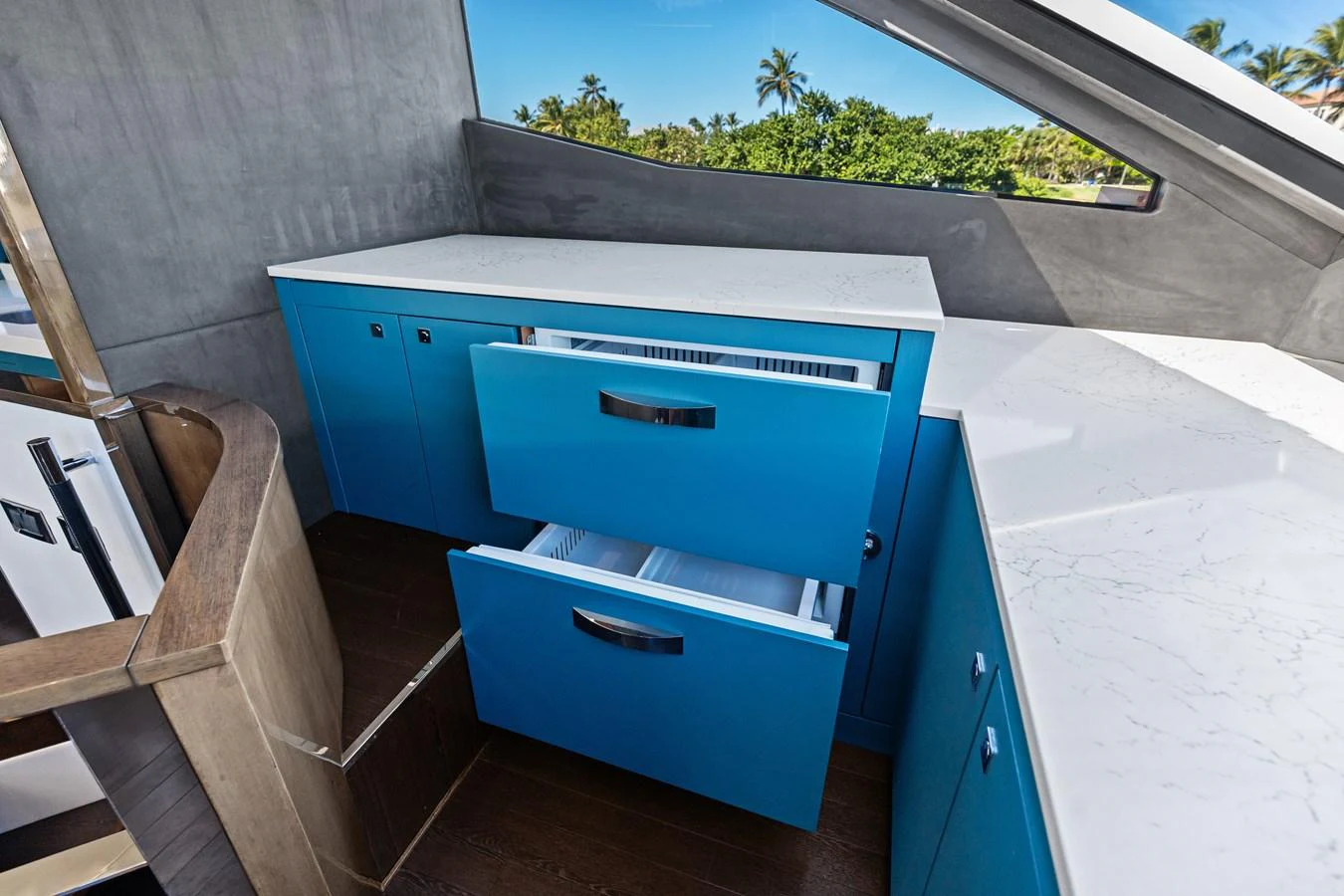 The yacht's galley features sleek blue cabinetry and modern appliances, set against a backdrop of lush greenery visible through large windows. aboard IT'S ENOUGH Yacht for Sale