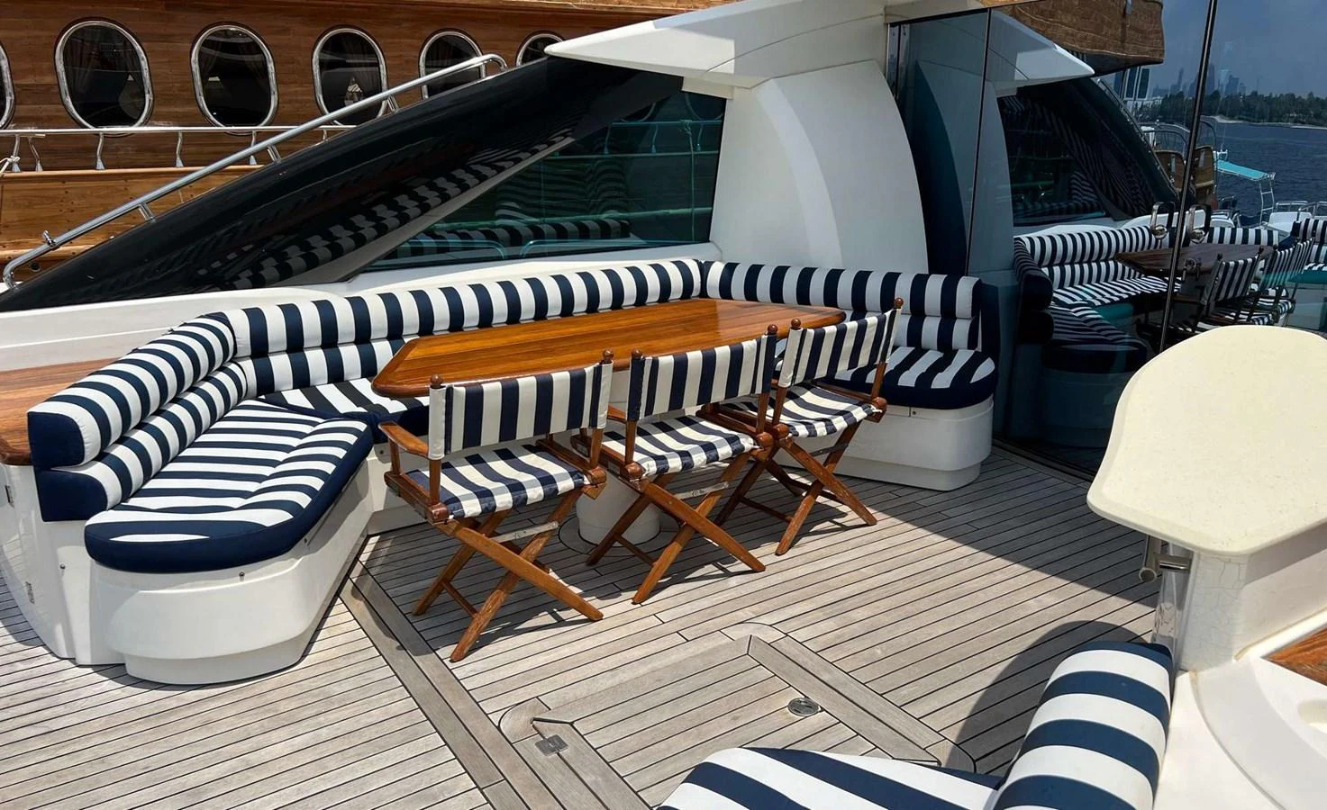 The aft deck features a stylish seating area with striped cushions and a wooden dining table, perfect for outdoor relaxation and dining. aboard TIMELESS C Yacht for Sale