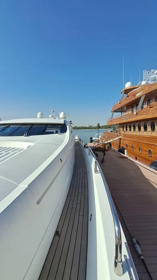 A sleek yacht is docked alongside a wooden yacht under a clear blue sky. aboard TIMELESS C Yacht for Sale