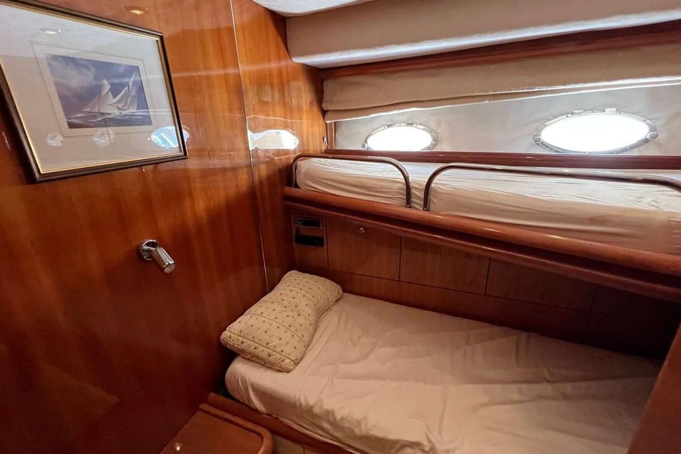 A cozy cabin with wooden paneling and two single beds, featuring a porthole window and framed artwork. aboard TIMELESS C Yacht for Sale