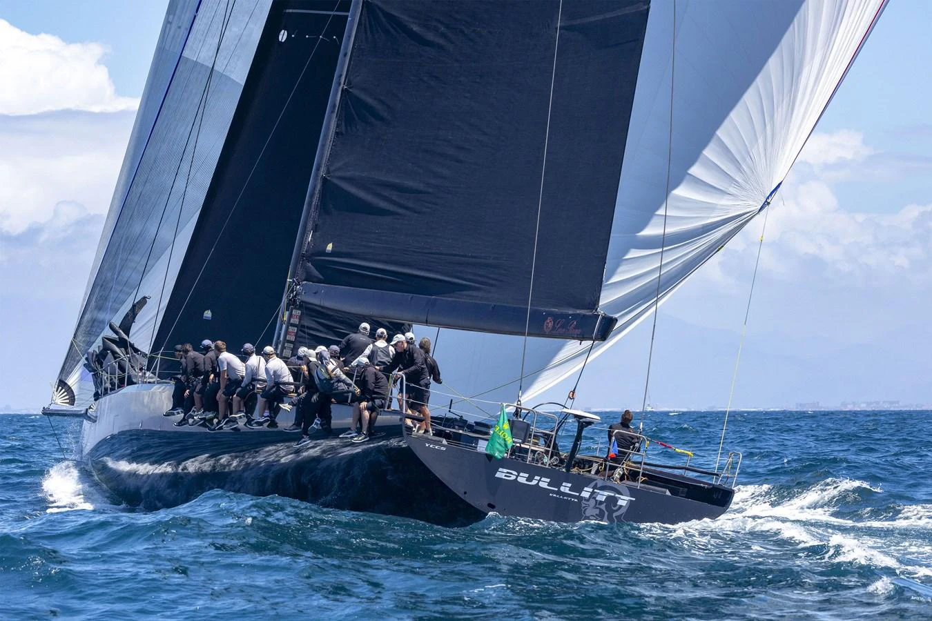 A sleek sailing yacht cuts through the waves with a crew actively managing the sails. aboard BULLITT Yacht for Sale
