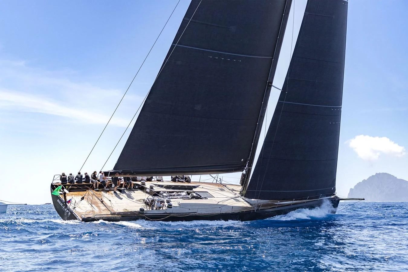 A sleek sailing yacht glides through the water with its sails fully extended and crew on deck. aboard BULLITT Yacht for Sale