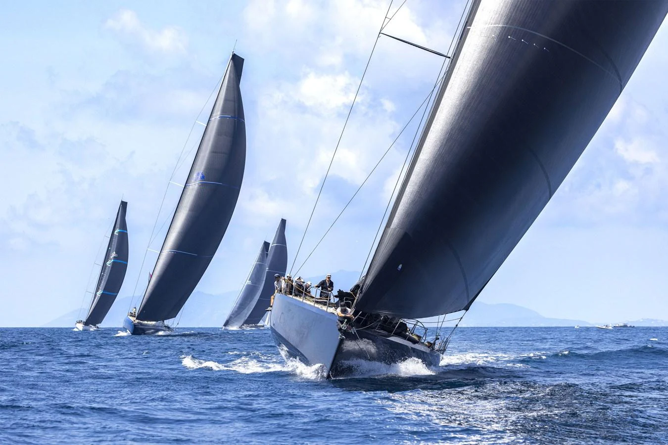 A sleek sailing yacht glides through the water with its sails fully extended, accompanied by other yachts in the background. aboard BULLITT Yacht for Sale