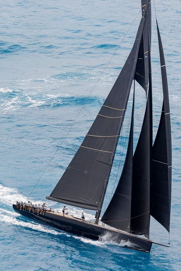 A sleek sailing yacht glides gracefully through the open sea with its black sails fully extended. aboard BULLITT Yacht for Sale