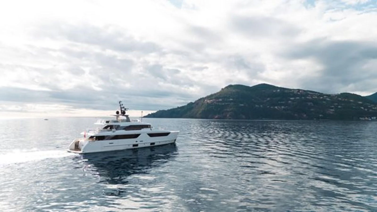 A sleek yacht cruises gracefully on calm waters with a scenic mountainous backdrop. aboard 2022 SANLORENZO SD118 Yacht for Sale
