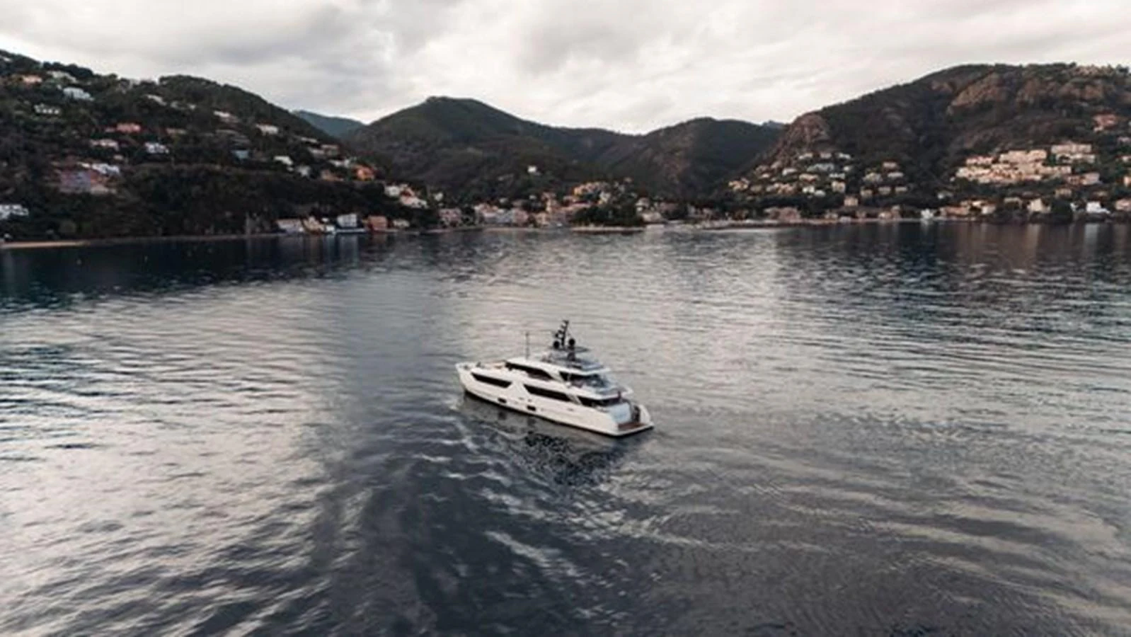 A sleek yacht cruises through calm waters with a scenic coastal backdrop. aboard 2022 SANLORENZO SD118 Yacht for Sale
