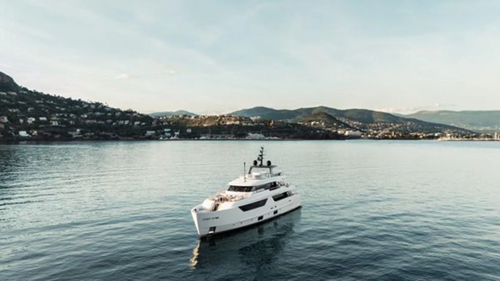 A luxurious yacht cruises serenely on calm waters with a scenic coastal backdrop. aboard 2022 SANLORENZO SD118 Yacht for Sale