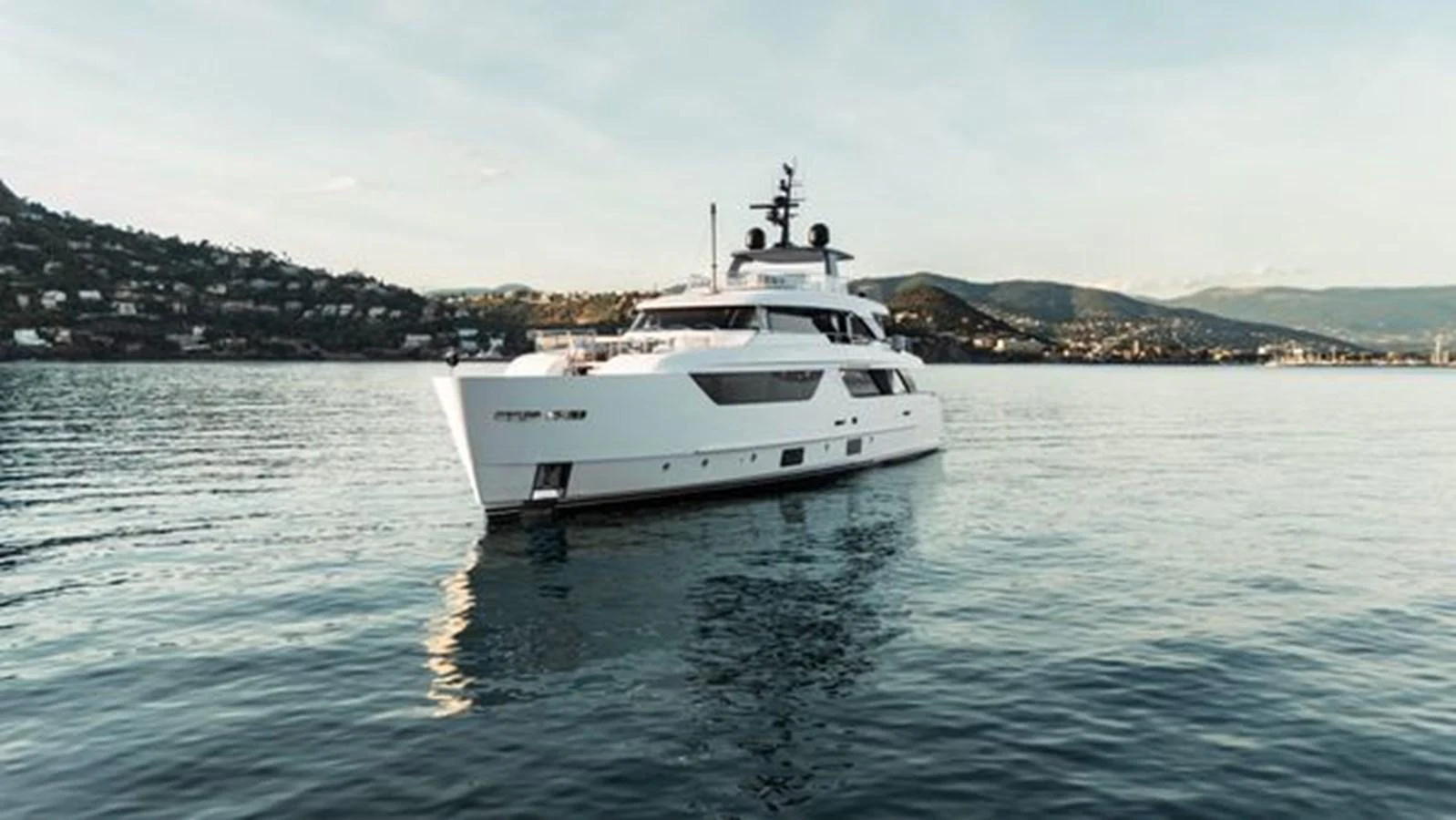 A sleek white yacht cruises through calm waters against a scenic backdrop. aboard 2022 SANLORENZO SD118 Yacht for Sale