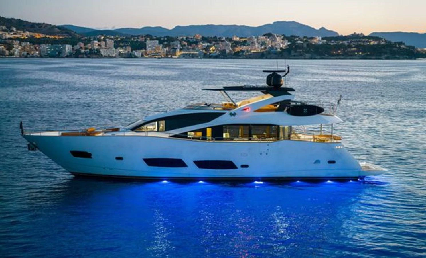 A sleek and modern yacht glides gracefully on the water, illuminated by vibrant blue underwater lights. aboard 2015 SUNSEEKER 28M RIII Yacht for Sale