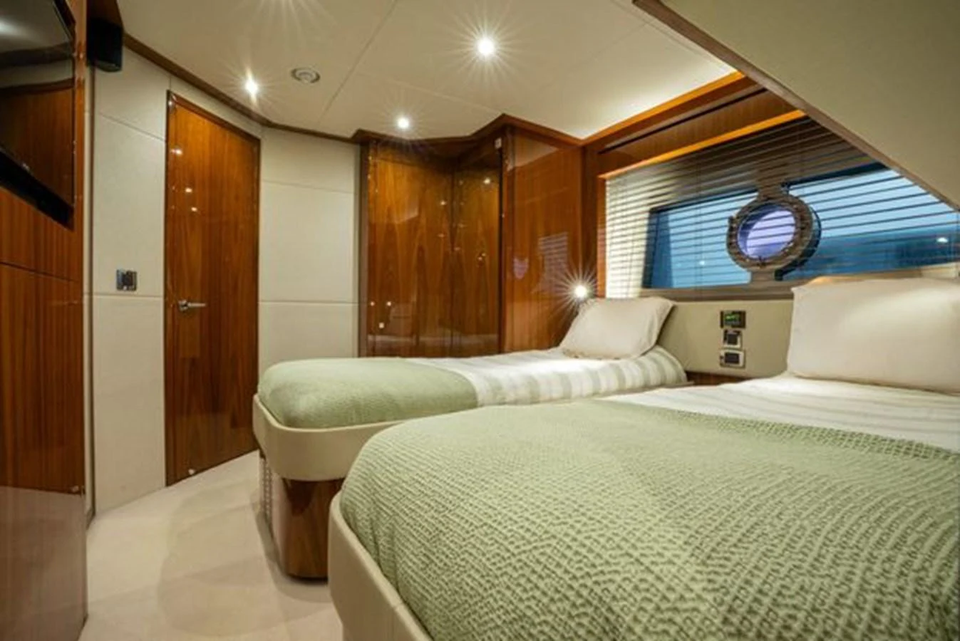 The guest stateroom features twin beds, warm wood finishes, and a porthole window for natural light. aboard 2015 SUNSEEKER 28M RIII Yacht for Sale