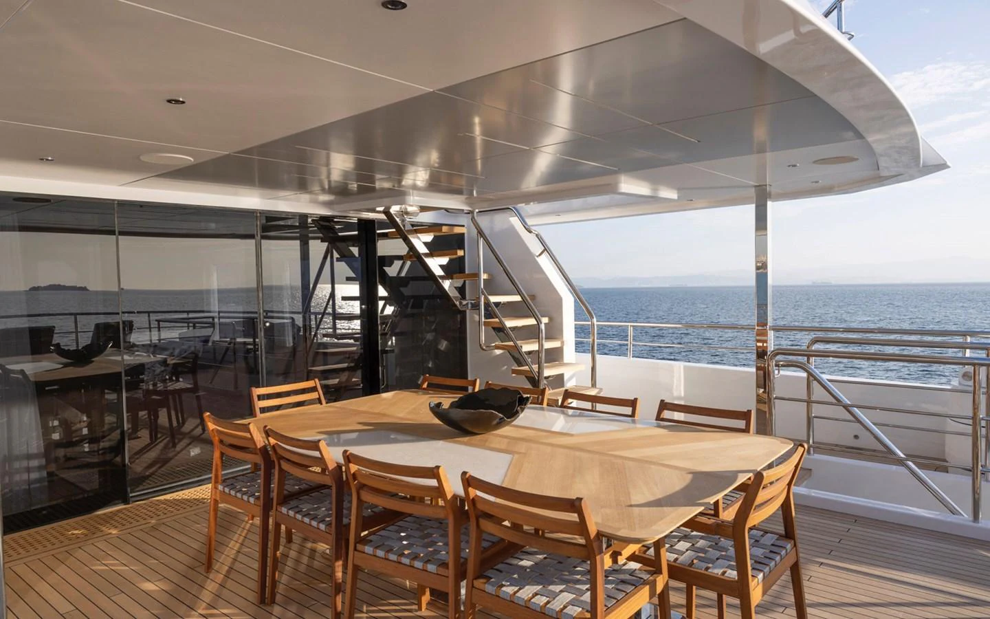 The aft deck features a spacious dining area with a large table and wooden chairs, perfect for al fresco meals with a view of the sea. aboard BEE EXPLORER YACHT Yacht for Sale