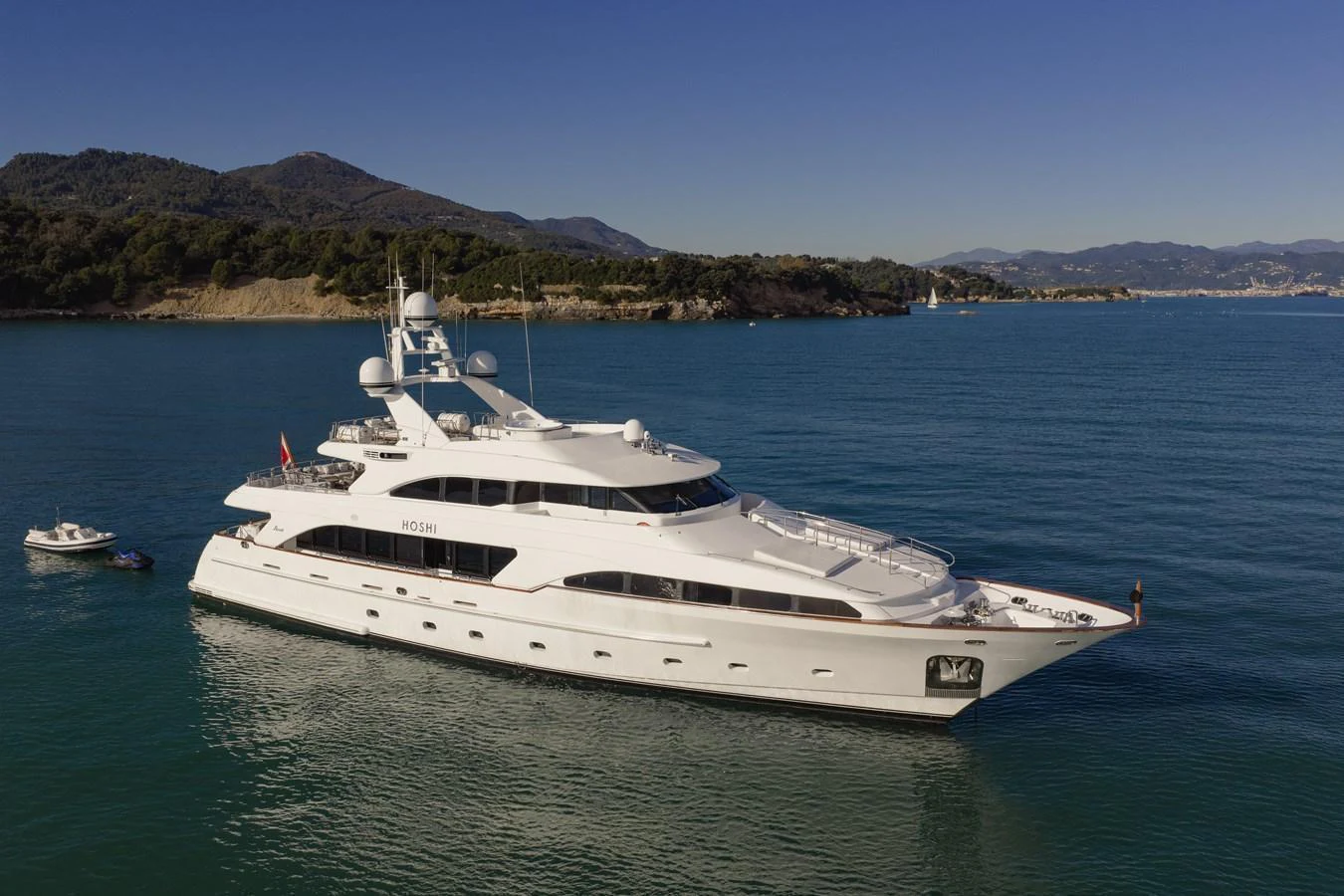 A luxurious yacht is anchored in serene blue waters with a picturesque coastline in the background. aboard HOSHI Yacht for Sale