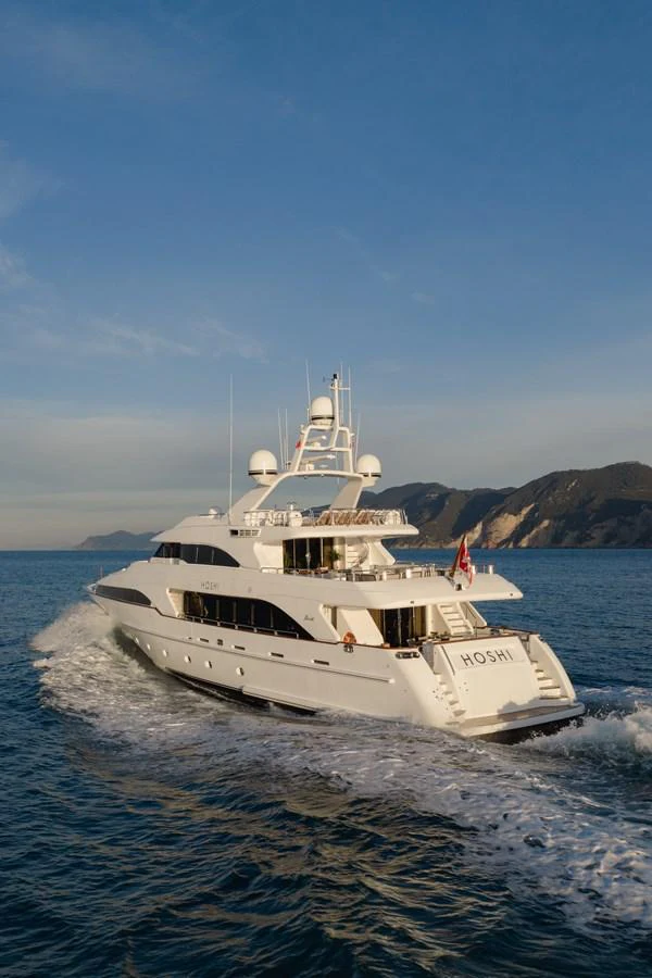 A luxurious yacht cruises through serene waters with a picturesque coastline in the background. aboard HOSHI Yacht for Sale