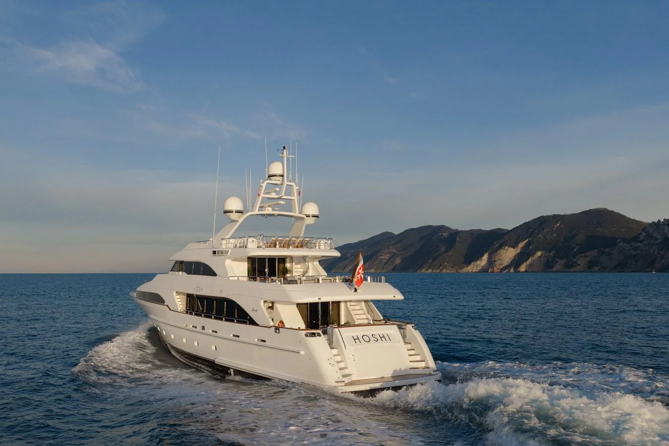 A luxurious yacht cruises through serene waters with a picturesque coastline in the background. aboard HOSHI Yacht for Sale