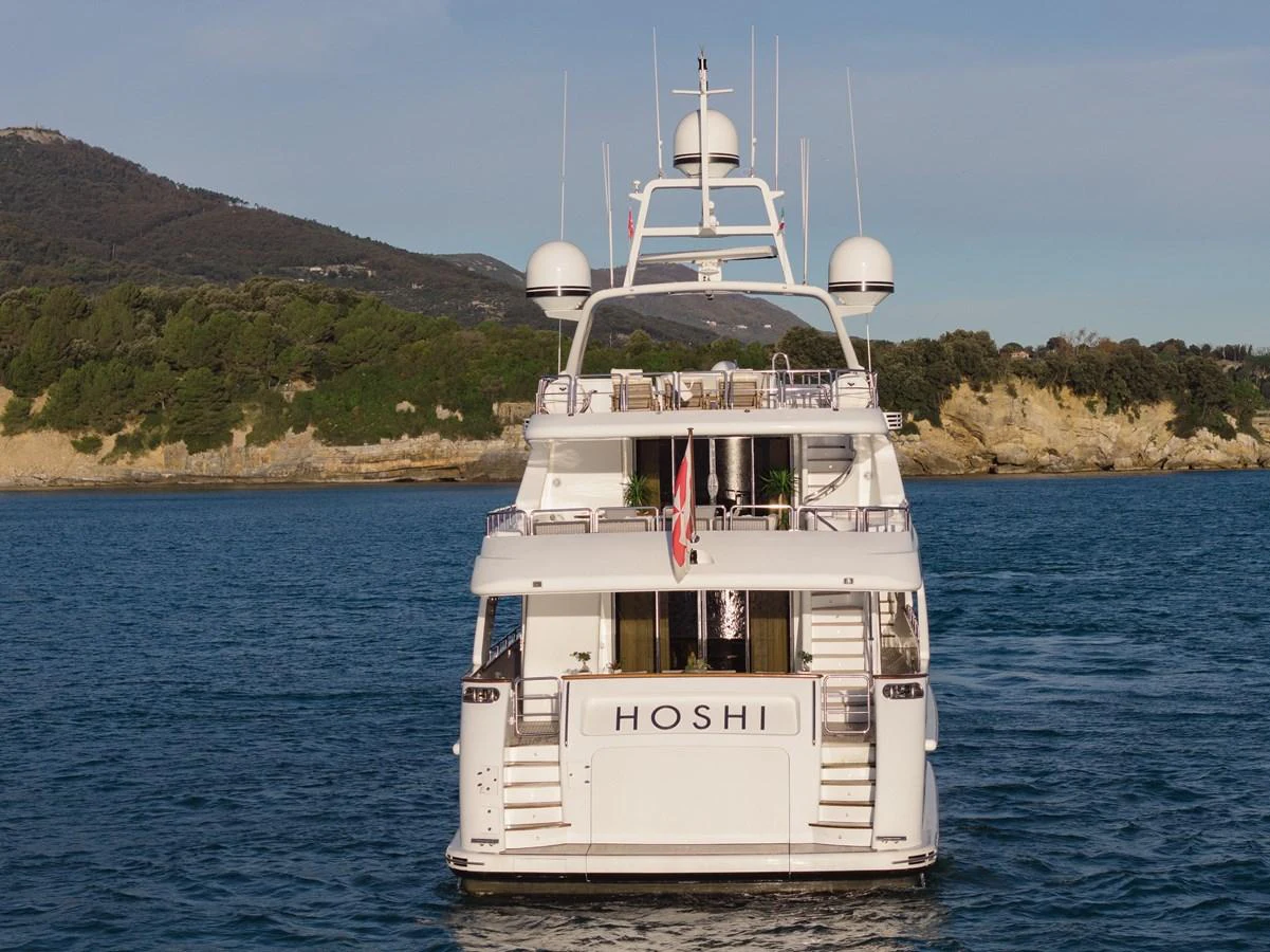A luxurious yacht is anchored in calm waters with a scenic coastal backdrop. aboard HOSHI Yacht for Sale