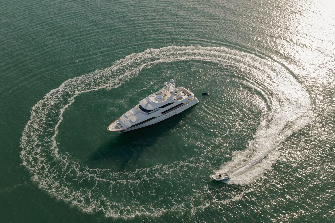 A luxurious yacht is captured from above, surrounded by a circular wake created by a smaller boat. aboard HOSHI Yacht for Sale
