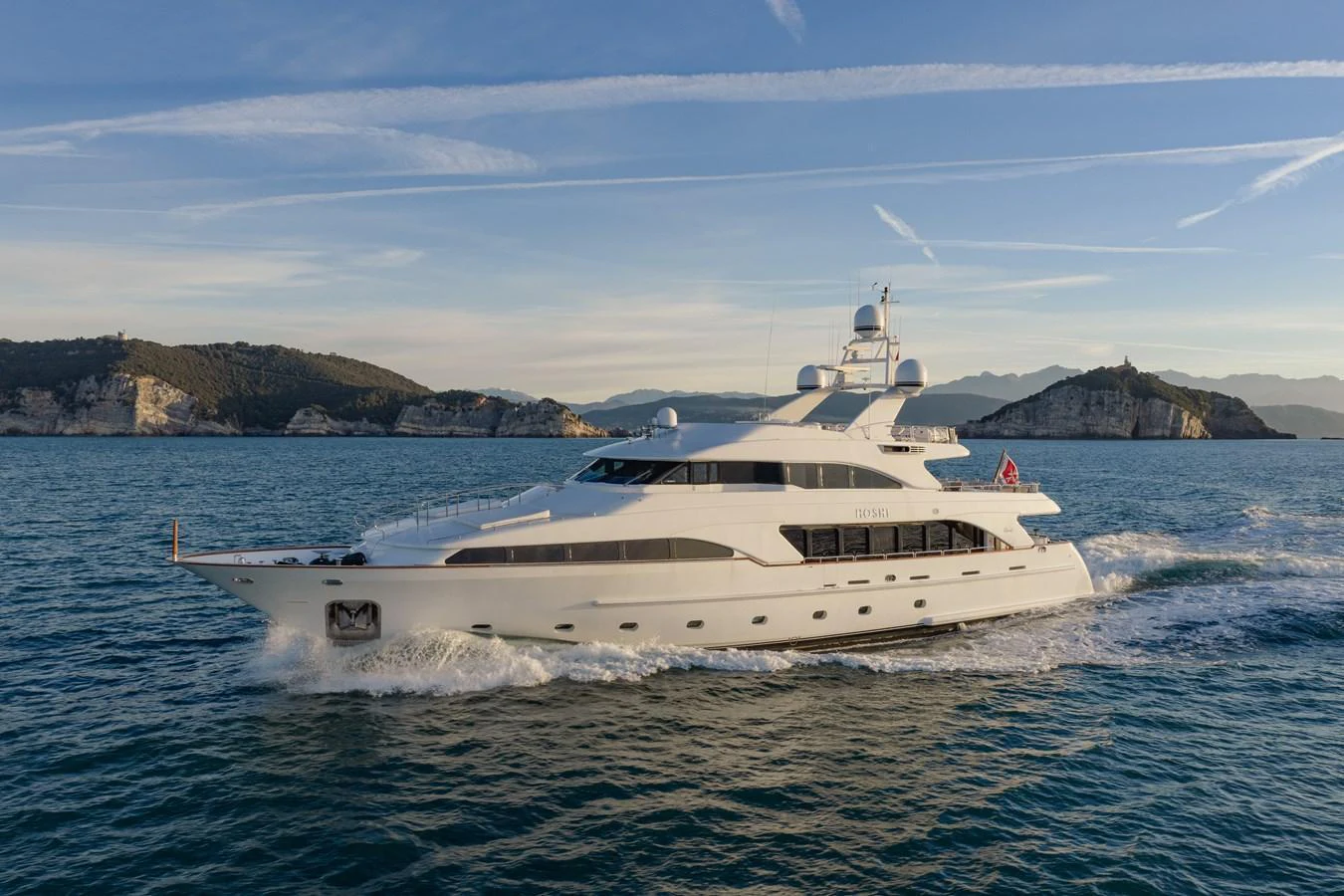 A luxurious yacht cruises through serene waters with a picturesque coastal backdrop. aboard HOSHI Yacht for Sale