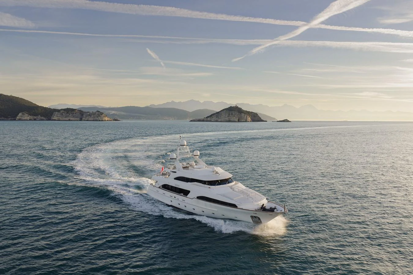 A stunning yacht cruises gracefully on the open sea with a picturesque backdrop of islands and mountains. aboard HOSHI Yacht for Sale