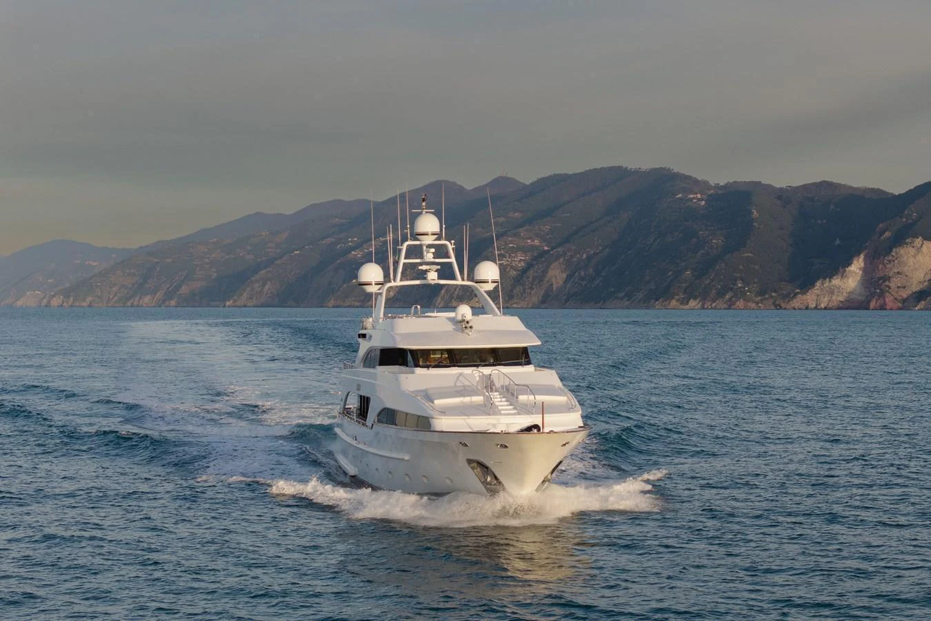 A sleek yacht cruises through calm waters with a scenic mountainous backdrop. aboard HOSHI Yacht for Sale