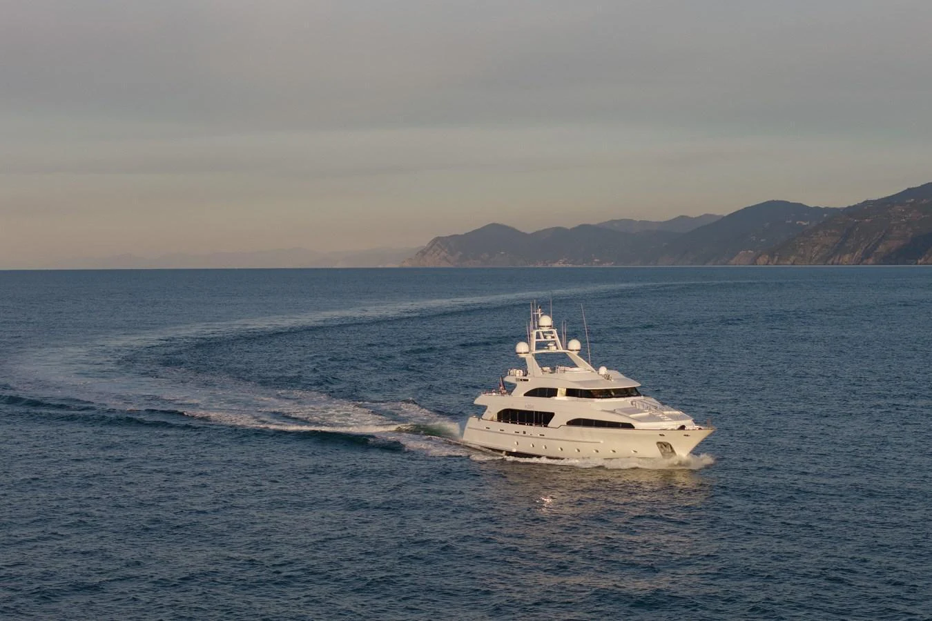 A luxurious yacht cruises gracefully on the open sea with a scenic coastline in the background. aboard HOSHI Yacht for Sale