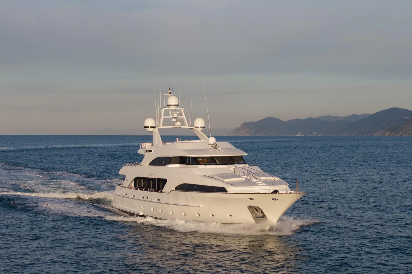 A luxurious yacht cruises through calm waters with a scenic coastline in the background. aboard HOSHI Yacht for Sale