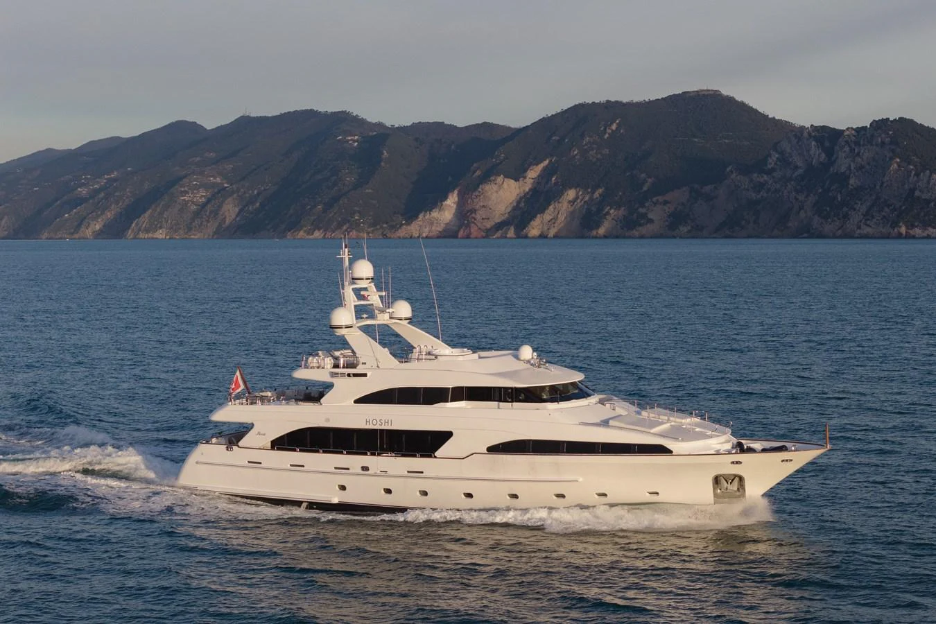A luxurious yacht cruising on calm waters with a scenic mountainous backdrop. aboard HOSHI Yacht for Sale