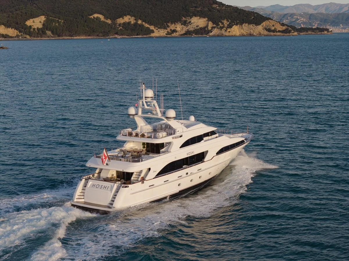 A luxurious yacht cruises through serene waters with scenic hills in the background. aboard HOSHI Yacht for Sale