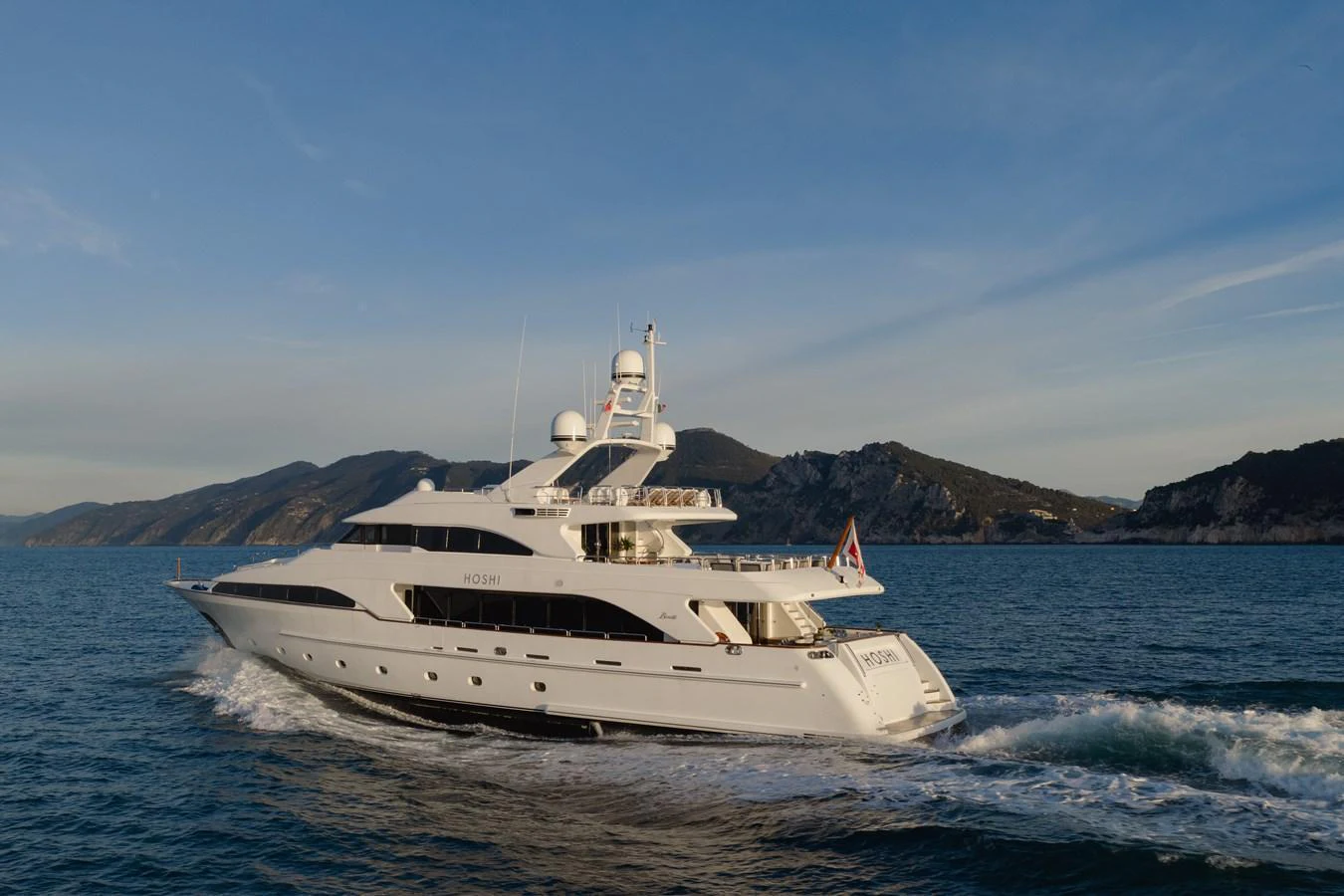 A sleek and elegant yacht cruising through calm waters with a scenic mountainous backdrop. aboard HOSHI Yacht for Sale