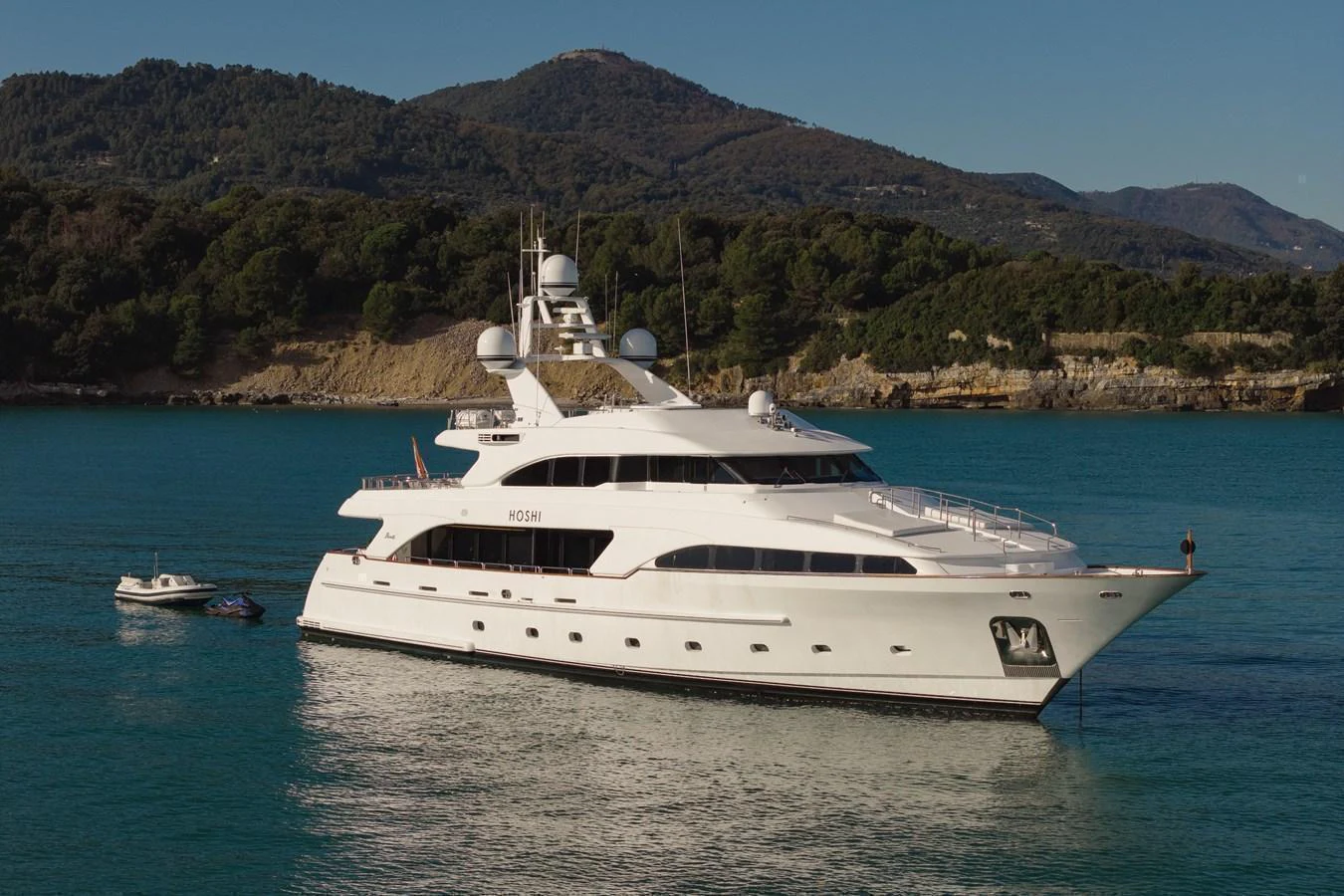 A luxurious yacht is anchored in a serene bay with picturesque hills in the background. aboard HOSHI Yacht for Sale