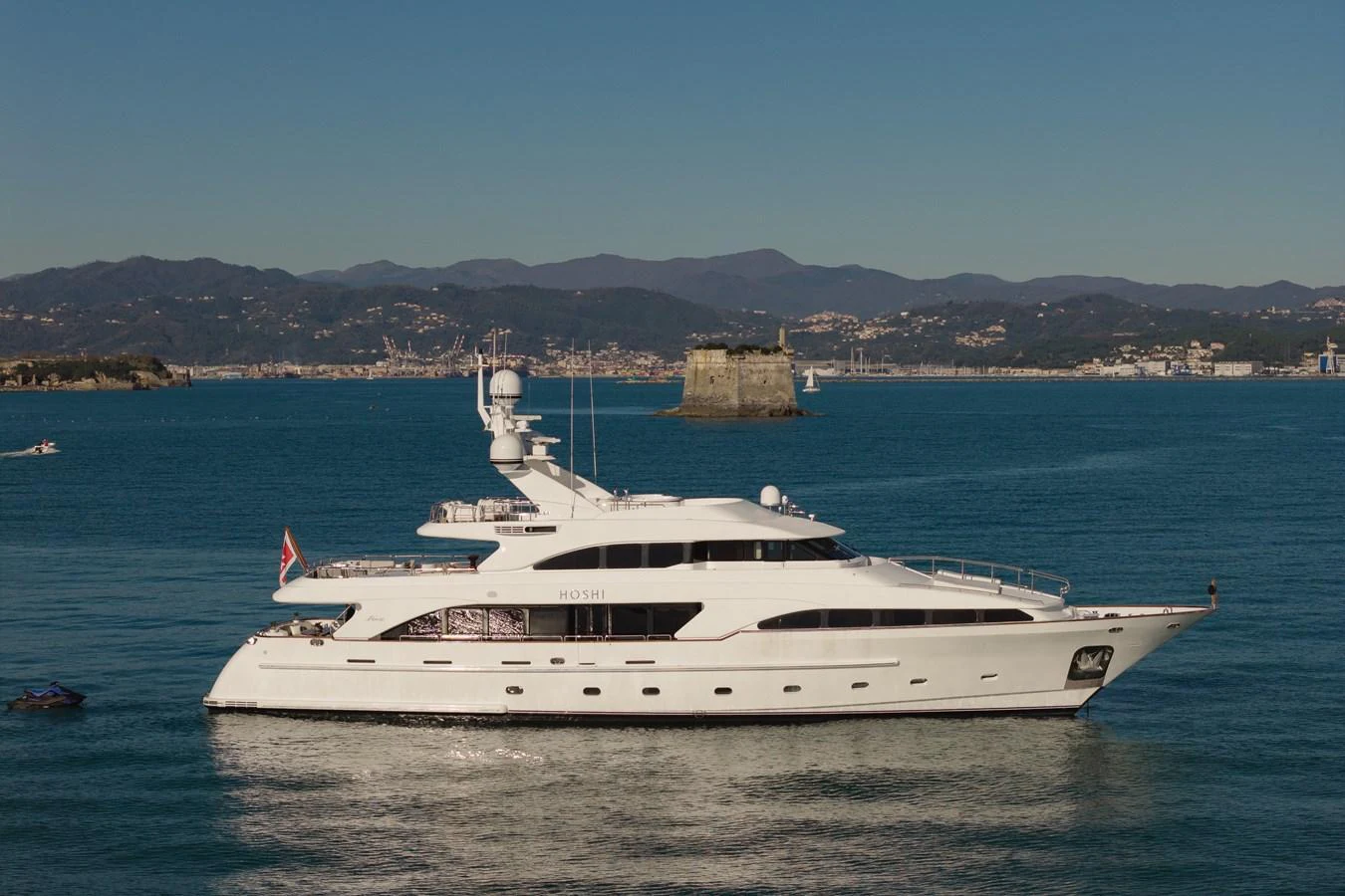 A sleek, modern yacht glides gracefully on calm waters with a scenic coastal backdrop. aboard HOSHI Yacht for Sale